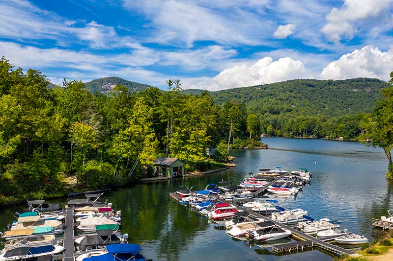 This is a view of Lake Toxaway. Boats are in the water and there are mountains surrounding the lake